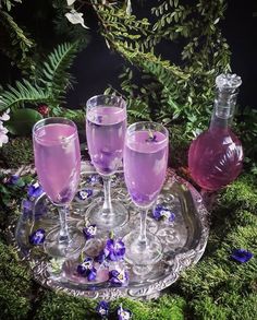 three wine glasses on a tray with purple flowers and greenery in the back ground