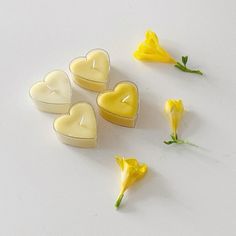 some yellow flowers and two heart shaped candles on a white surface with one candle in the shape of a heart