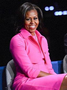 the first lady in pink suits is sitting on a chair with her legs crossed and smiling