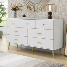 a white dresser with gold handles and drawers in front of a wallpapered wall