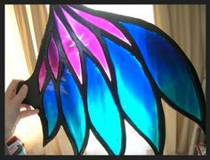 a hand holding up a stained glass lamp with blue and pink feathers on it's side