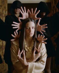 a woman with hands on her head in front of two other women wearing black hoods