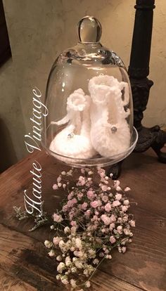 a glass clochet with two baby shoes under it and flowers on the table