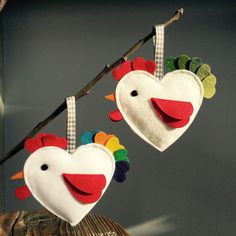 two heart shaped felt ornaments hanging from a tree branch in the shape of roosters