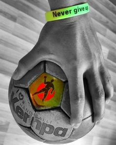 a person's hand holding a soccer ball with a wristband that says never give it