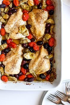 a white dish filled with chicken, olives and tomatoes