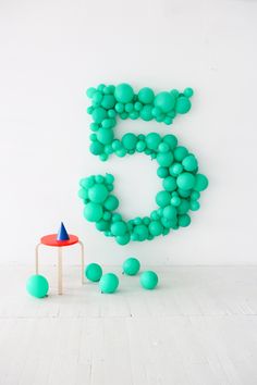 a young boy sitting on a stool in front of a number 5 balloon wall with green balls