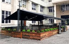 an outdoor seating area in front of a large building with lots of windows and plants