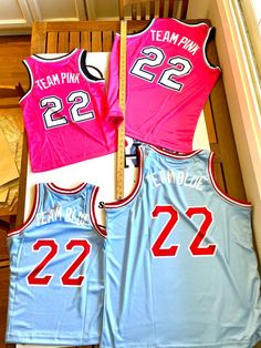 three pink and blue basketball jerseys sitting on top of a wooden bench next to each other