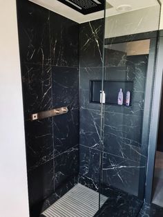 a walk in shower sitting next to a black tiled wall and floor covered in marble