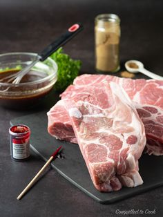 two raw meats sit on a cutting board with chopsticks and seasoning