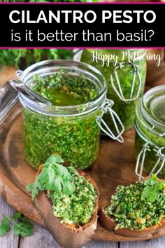 three jars filled with pesto on top of a wooden tray next to bread and parsley