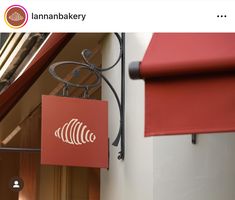 a red sign hanging from the side of a building next to a window with an awning