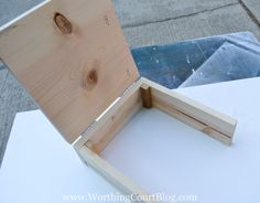 an open wooden box sitting on top of a white table next to a piece of wood