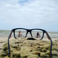 two people riding bikes on the beach with their reflection in them's eyeglasses