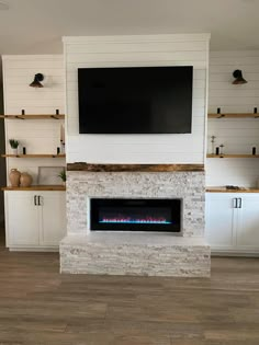 a tv mounted on the wall above a fireplace in a living room with white cabinets