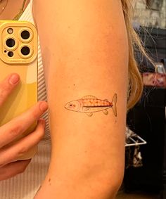 a woman with a fish tattoo on her arm holding a cell phone and looking at the camera