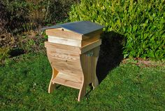 a wooden beehive sitting in the grass next to a bush and shrubbery