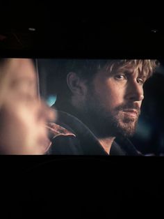 a man driving in the dark with his hand up and looking at something on the screen