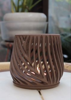 a brown candle holder sitting on top of a white table next to potted plants