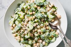 a white bowl filled with cucumber and chickpeas next to a spoon