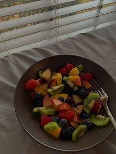 a bowl filled with cut up fruit on top of a bed next to a window