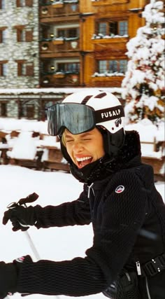 a young man riding skis on top of snow covered ground with buildings in the background