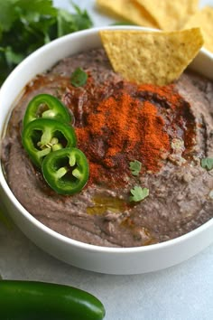 a white bowl filled with black bean dip surrounded by chips and jalapenos