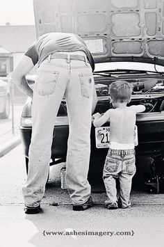 an older man standing next to a little boy in front of a car with the hood open