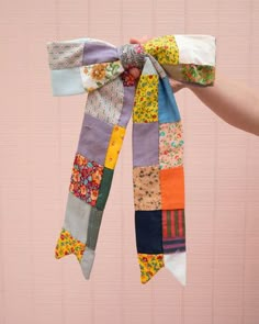 a person holding up a multicolored patchwork scarf with a bow on it