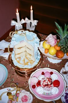 a table topped with plates and cakes covered in frosting next to two lit candles