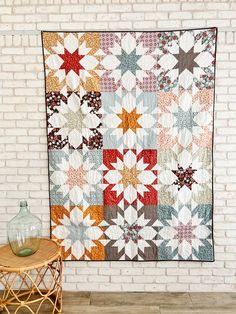 a quilt hanging on the wall next to a table with a vase and glass jar