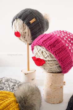 two knitted hats sitting on top of a wooden stand next to yarn balls and needles