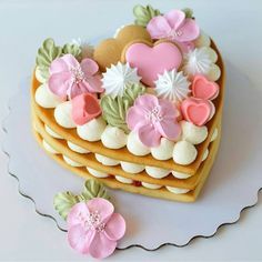 there is a heart shaped cake with flowers on the top and two cookies in the shape of hearts