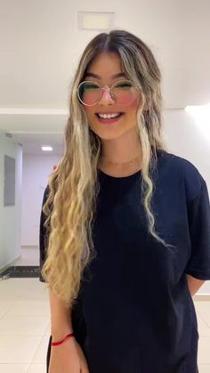 a woman with long blonde hair and glasses smiling at the camera while standing in an empty room