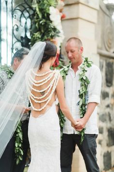 a bride and groom holding hands at their wedding ceremony in front of an arch with greenery