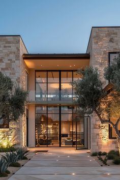 the entrance to a modern home with stone walls and glass doors at night time, surrounded by greenery