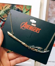 the avengers necklace is being held up in front of a card with an arrow on it