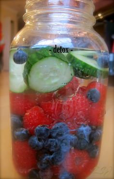 a jar filled with blueberries, cucumbers and raspberries on top of a table