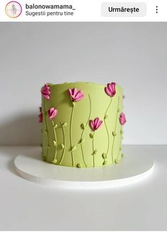 a green cake with pink flowers on it sitting on top of a white countertop