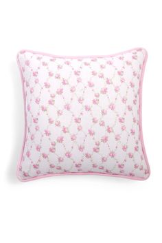 a pink and white pillow with flowers on the front, sitting on a white surface