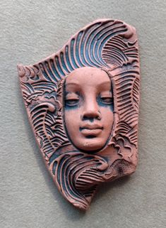 a clay face is mounted on the wall, with intricate designs and curves around it