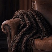 a brown chair with a blanket on top of it next to a leather chair and window