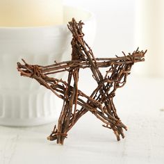 a star made out of twigs sitting next to a white bowl with a candle in it