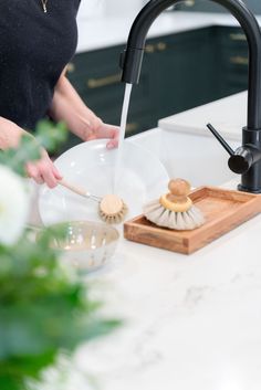 a woman is washing dishes in the kitchen sink with a wooden brush and soap dispenser