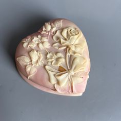 a pink heart shaped box with white flowers and leaves on the inside, sitting on a gray surface