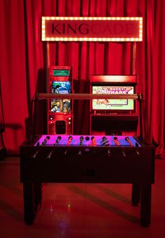 an arcade machine is lit up with neon lights in front of a red curtained background