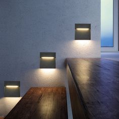 three square lights are lit up on the wall above a long wooden table and bench