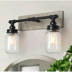 two mason jar lights are mounted on the wall above a mirror and vanity light fixture