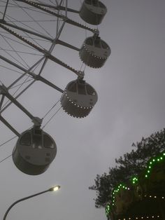 the ferris wheel is lit up with green lights on it's sides and some trees in the background